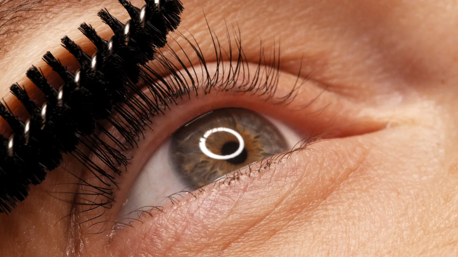 Close-up of an eye with lifted natural lashes and a lash wand